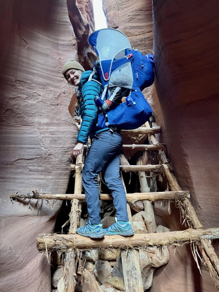 Hailey climbing down a ladder in Buckskin Gulch with her baby on her back
