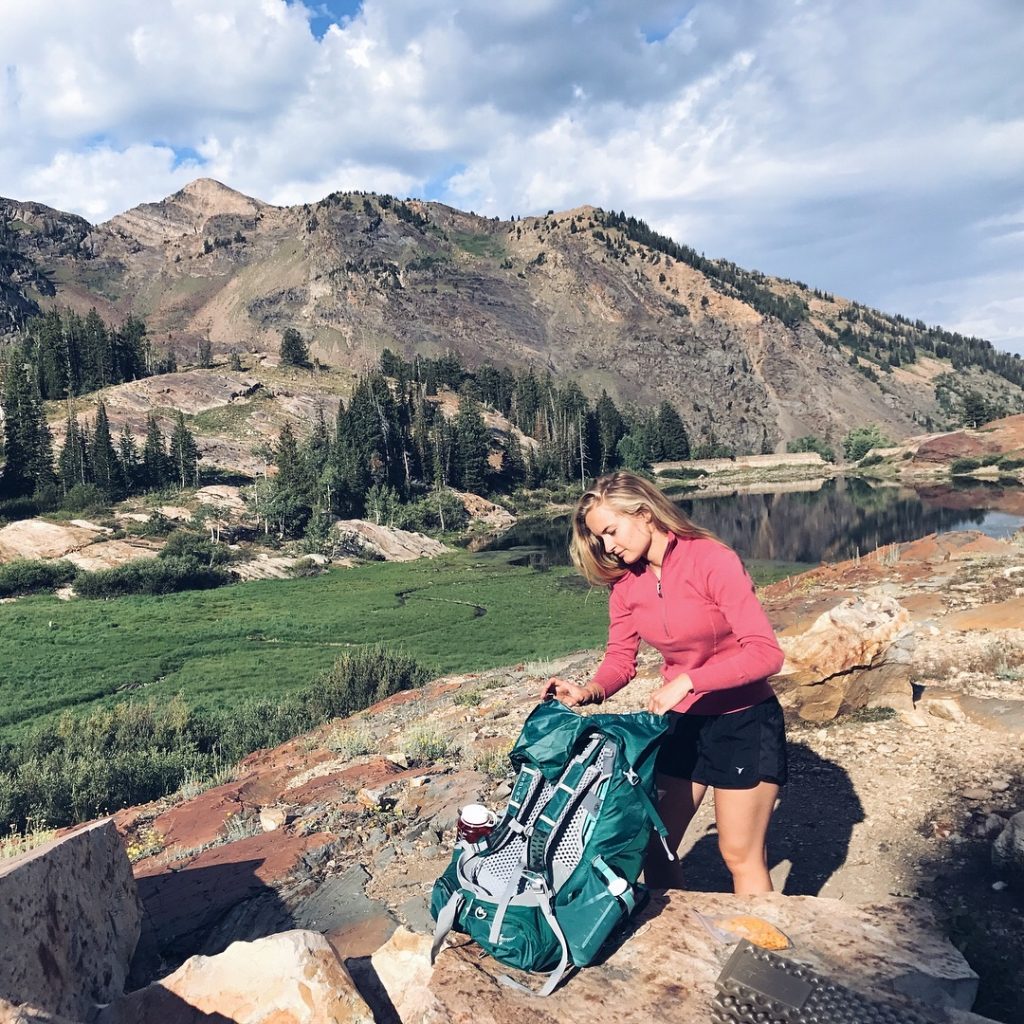 Hailey packing up her backpacking pack in front of a beautiful mountain and lake backdrop
