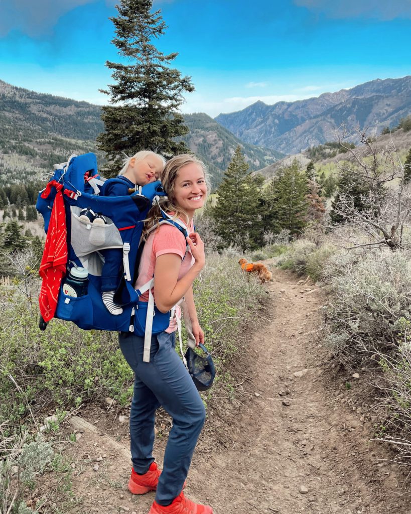 Hailey and her baby sleeping in the pack standing in front of beautiful utah mountain landscape