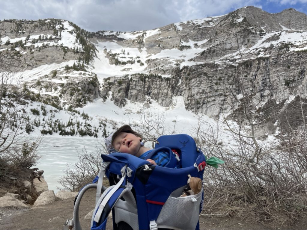 Hailey's baby sleeping in his pack in front of snowy mountain